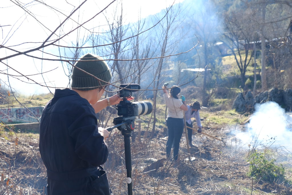 A videographer films people burning brush along a creek bed.